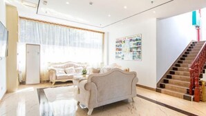 Un salon spacieux avec un canapé beige, une grande fenêtre ornée de rideaux légers, une affiche accrochée au mur et un escalier avec des rampes en bois.