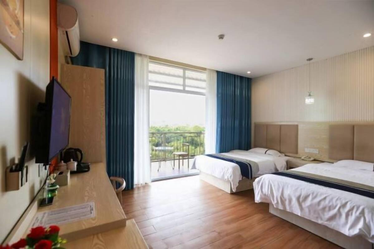 A hotel room with two beds, a desk with a computer, a TV, and a balcony with a view.