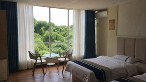 Une chambre d’hôtel avec une grande fenêtre, deux lits, une table avec des chaises et une vue sur la verdure.