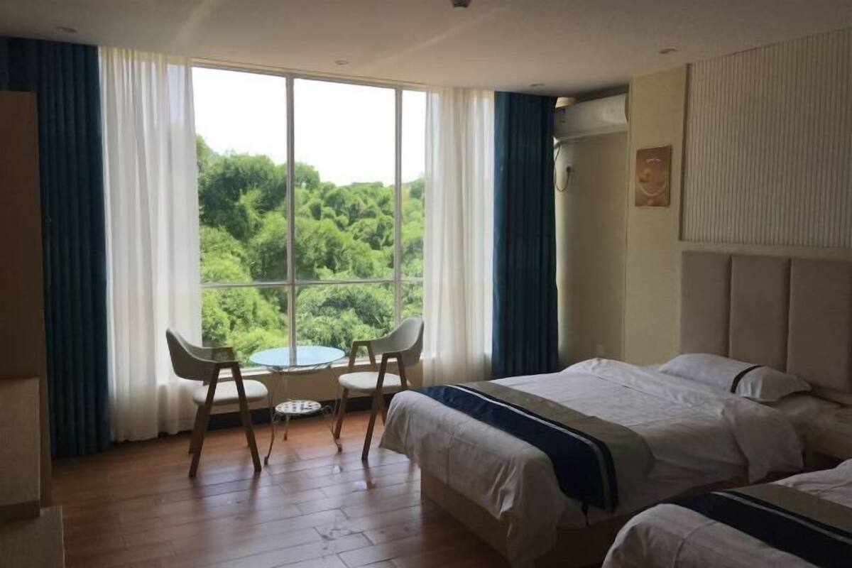 A hotel room with a large window, two beds, a table with chairs, and a view of greenery.
