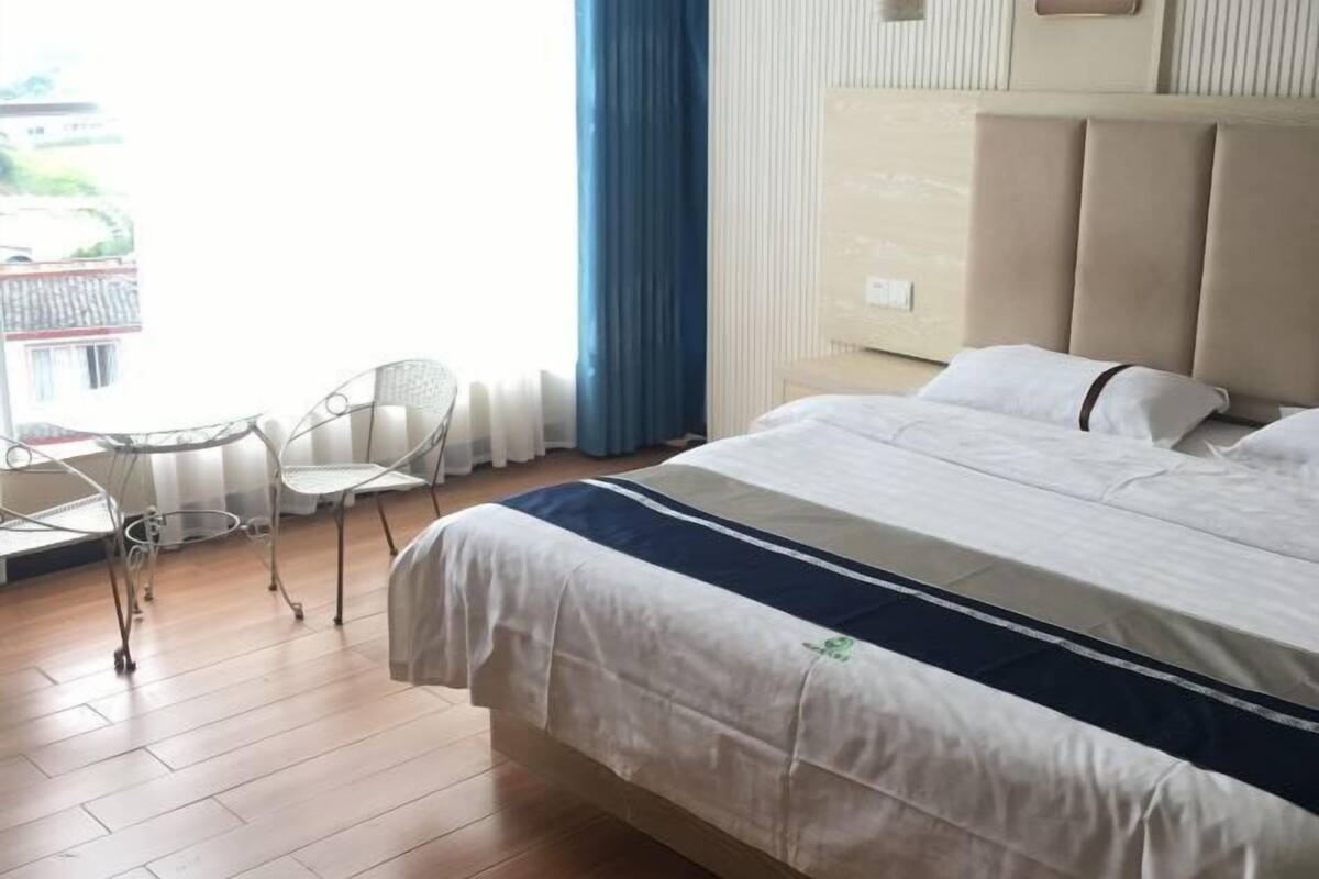 A hotel room with a bed, a chair, a small table, and a view of the outdoors.