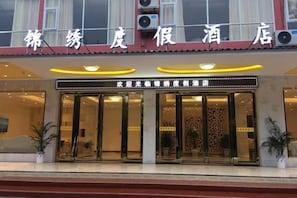 A hotel entrance with a sign above the doors, potted plants, and a clear view of the interior through the glass doors. - Jinxiu Holiday Hotel (Yangshuo)