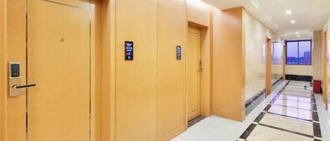A hotel corridor with wooden doors, a tiled floor, and a view through the windows.