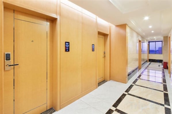 A hotel corridor with wooden doors, a tiled floor, and a view through the windows.