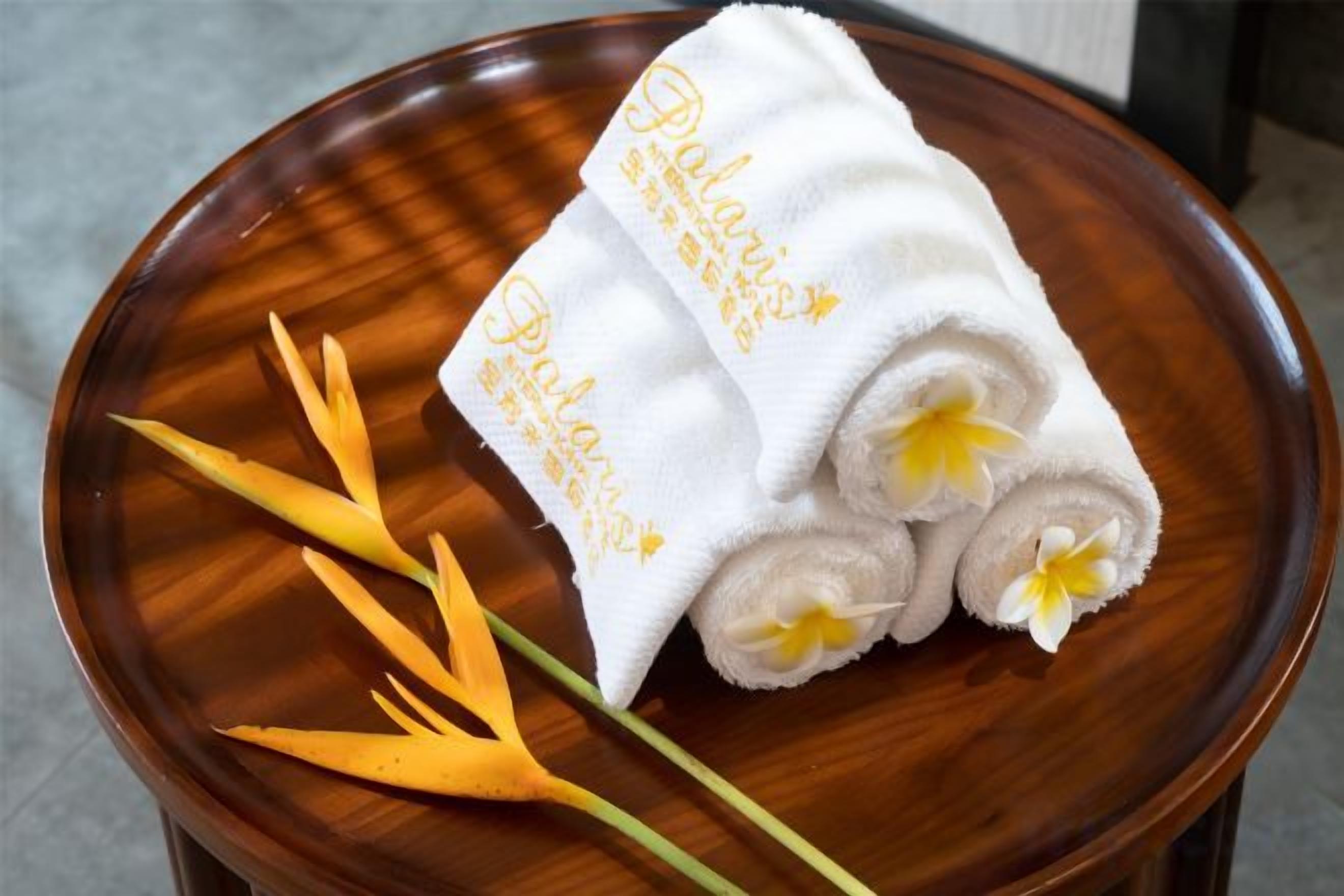 A wooden bowl containing rolled towels with a floral design, accompanied by a yellow flower.