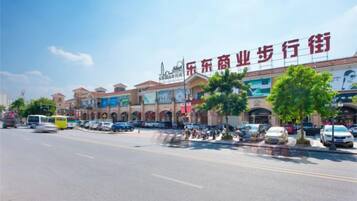 A commercial street with shops, parked cars, and a clear sky.