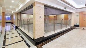 Un moderno vestíbulo de hotel con piso de mármol, barandales de vidrio y una recepción.