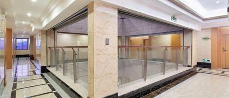 A hotel lobby with a marble floor, a glass elevator, and a reception desk.