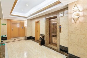 A hotel lobby with a marble floor, a reception desk, and an elevator. - Polaris International Hotel (Ledong)