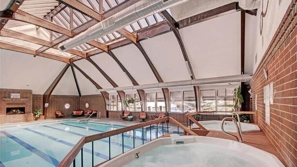 Une piscine intérieure dotée d’un jacuzzi, de poutres en bois et de murs en briques.