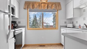 Une cuisine moderne avec des meubles blancs, une fenêtre donnant sur des arbres et un four à micro-ondes.