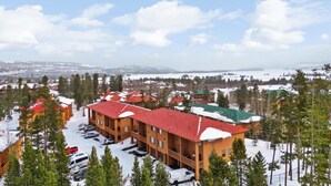 Un immeuble à plusieurs étages, doté d’un toit rouge, entouré d’arbres couverts de neige et d’un parking.