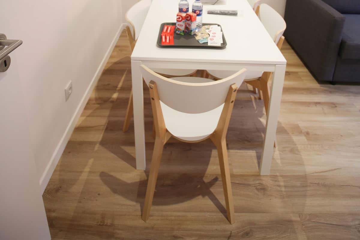 A dining area with a white table and chairs, a painting on the wall, and a grey sofa in the background.