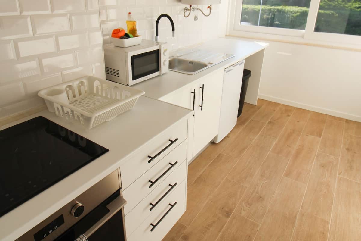 A modern kitchen with white cabinetry, a microwave, a sink, and a window with a view of greenery.