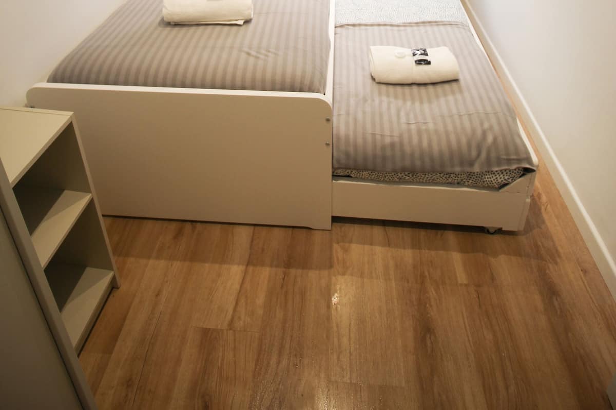 A small, single-bed room with a window, wooden flooring, and a white wardrobe.