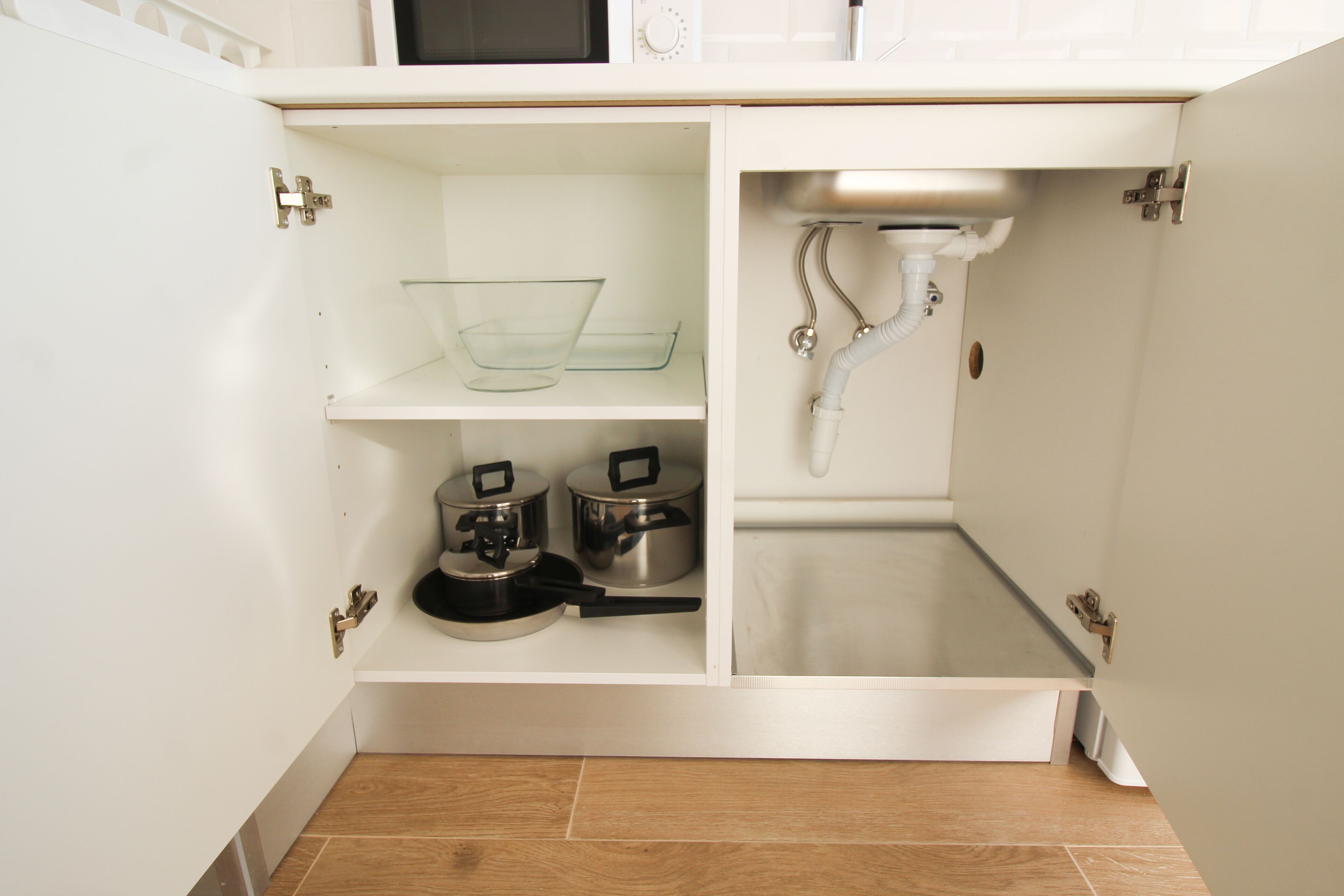 A kitchen with white cabinets, a microwave, a sink, and two pots.