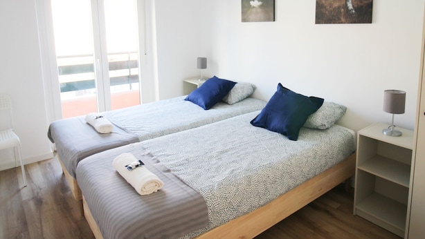 A modern bedroom with two beds, a balcony, and artwork on the walls. - ORIENTE DNA STUDIOS X (Loures)