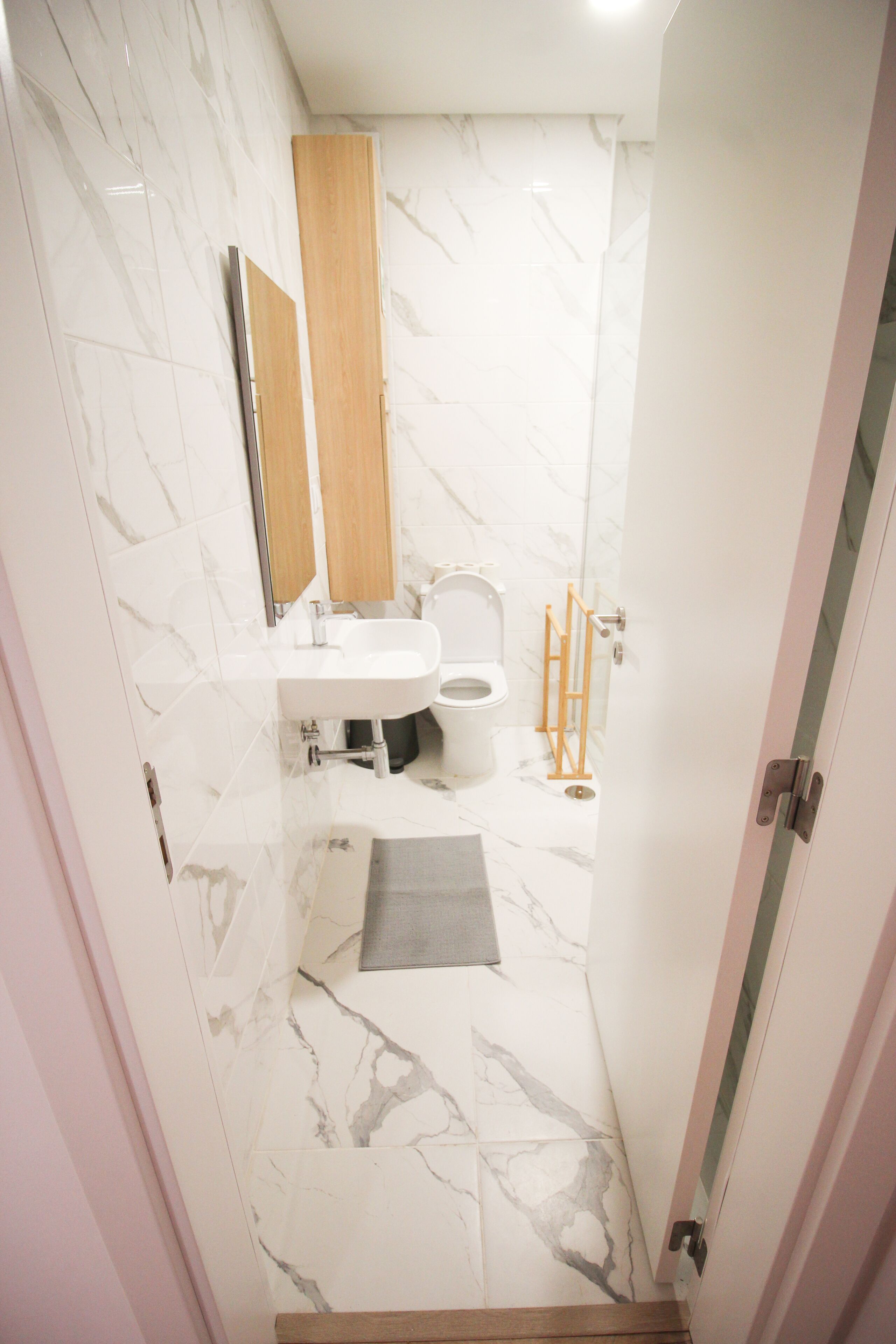 Une salle de bain avec un lavabo, un miroir et des toilettes blancs, des murs en marbre et un plancher en bois.