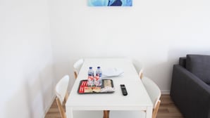 A white dining table with four chairs, a gray sofa, and a blue abstract painting on the wall. - ORIENTE DNA STUDIOS X (Loures)