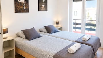 A hotel room with two beds, a wooden floor, and a balcony with a view.