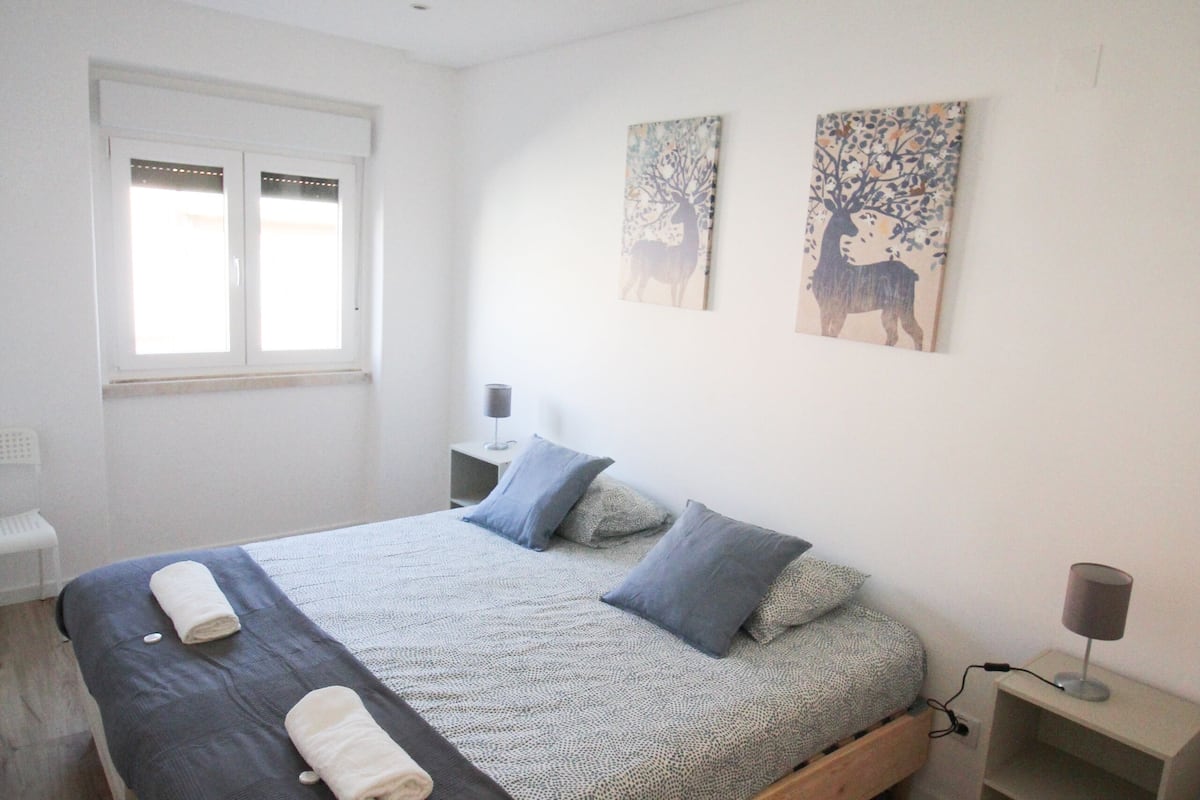 A bedroom with a wooden bed, a nightstand, a lamp, and artwork on the wall.