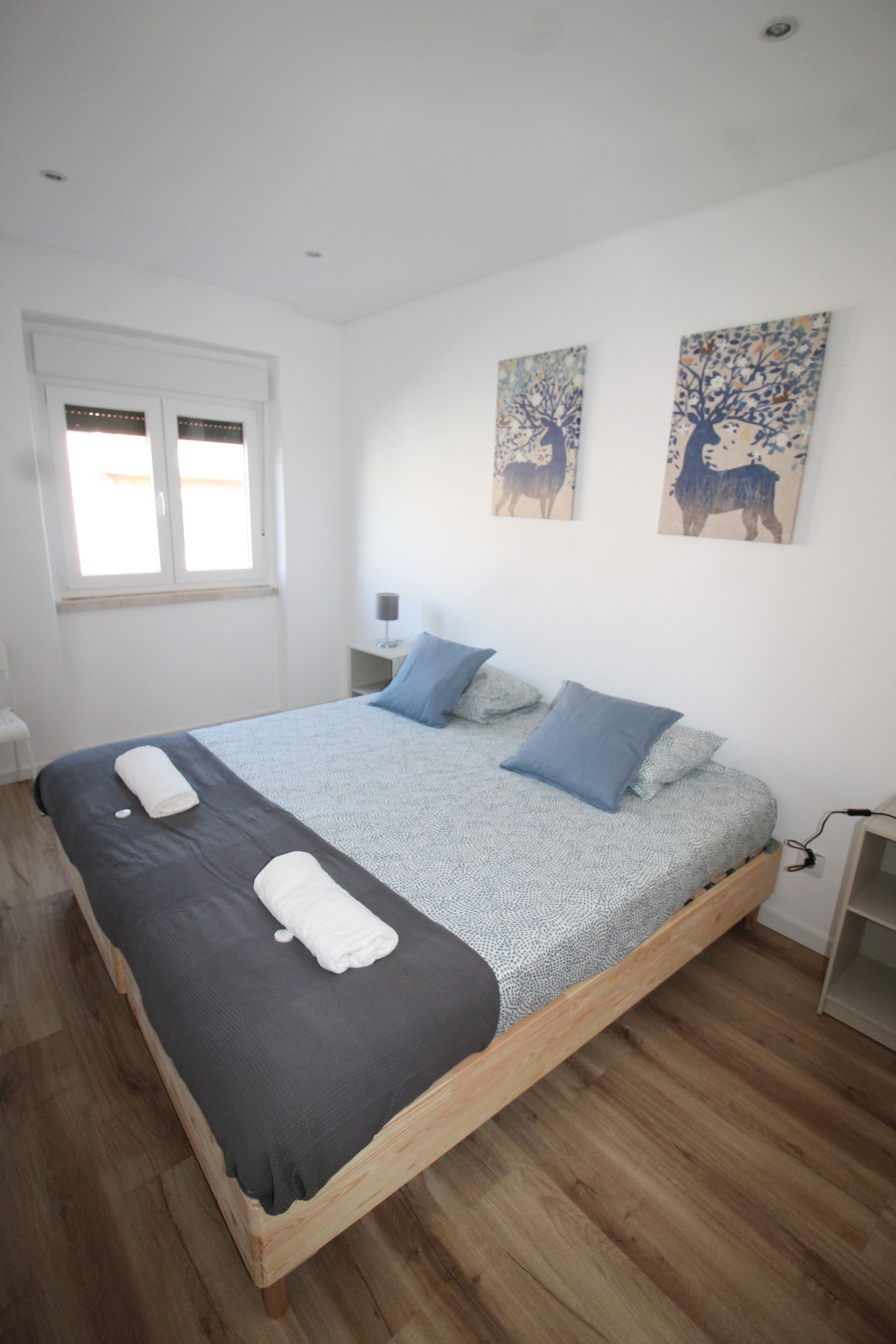A bedroom with a wooden bed, white walls, and two paintings on the wall.