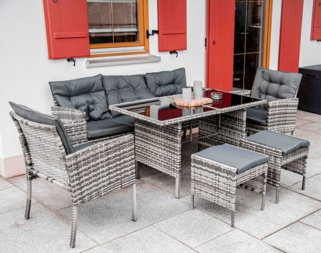 Un área de estar exterior de mimbre con un sofá y dos sillones, una mesita y una mesa auxiliar.