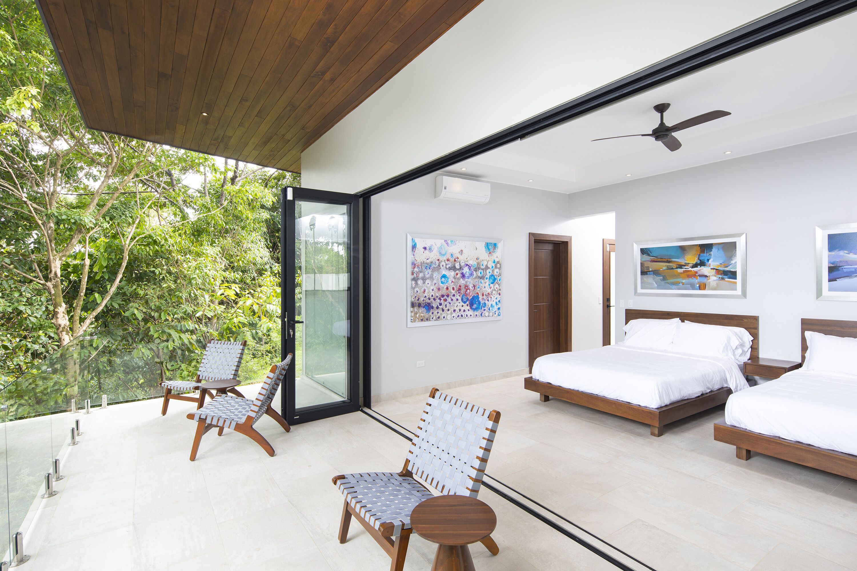 A modern bedroom with a large bed, a smaller bed, a chair, and a ceiling fan.