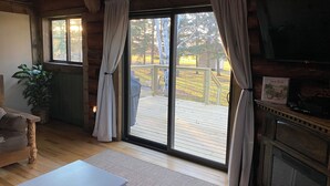 Accogliente interno di una baita con pavimento in legno, un tavolo bianco, un camino e un'ampia porta-finestra che si apre su un patio.