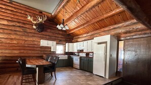 Interno di una baita in legno con zona pranzo, cucina e un'ampia porta di legno.