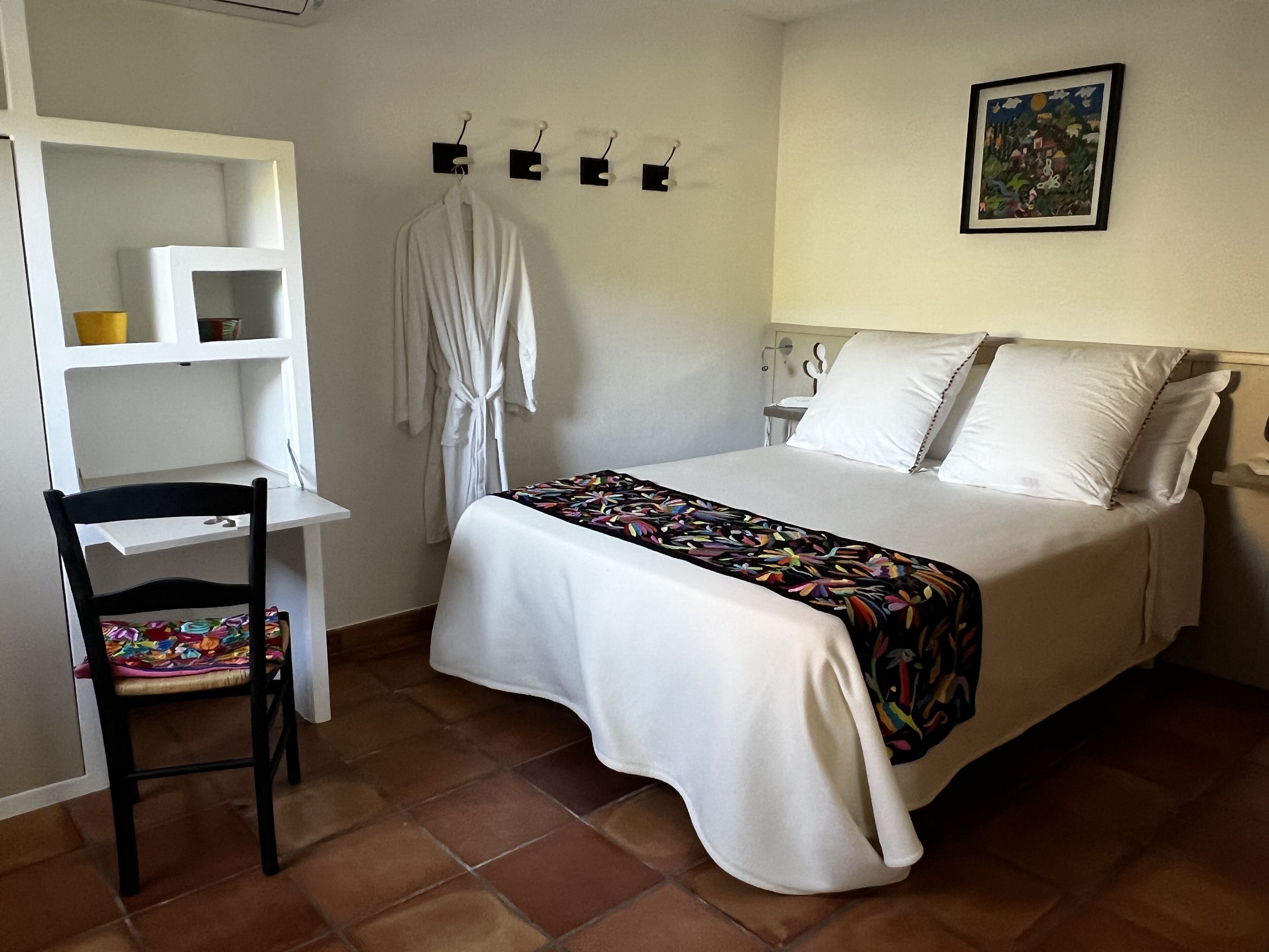 A bedroom with a bed, a chair, a desk, and a wall-mounted shelf.