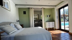 Ein Schlafzimmer mit einem Bett, einem Nachttisch, einem durchgehenden Türspalt sichtbaren Badezimmer und Blick auf einen Pool im Freien.
