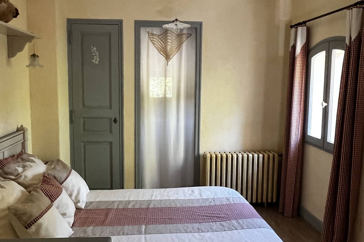 A bedroom with a bed, a radiator, a door, and a window with curtains.