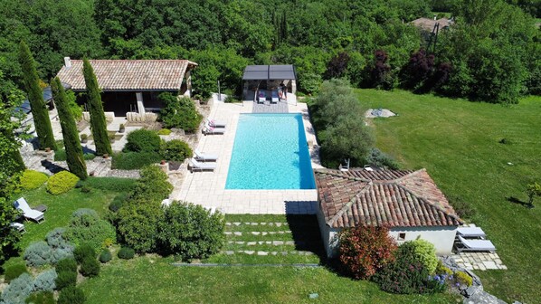 An aerial view of a property with a swimming pool, lounge chairs, and a garden.