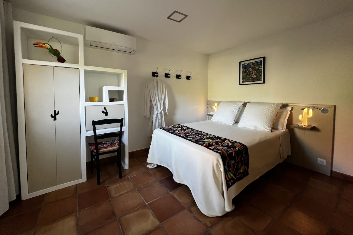 A bedroom with a bed, a wardrobe, a chair, a robe, and a nightstand with a lamp.