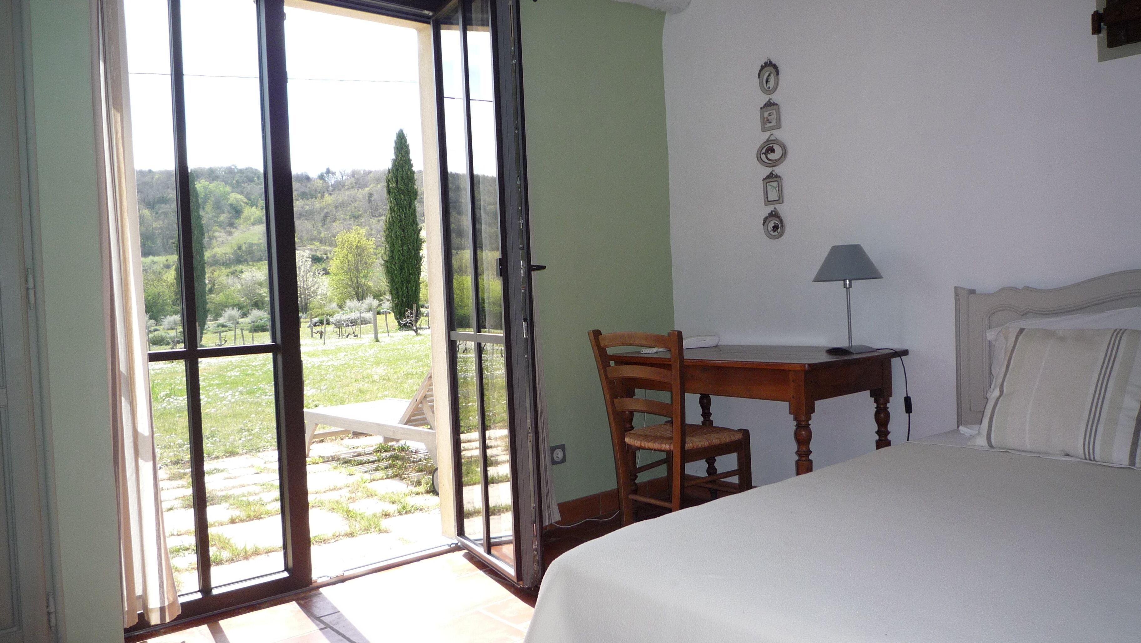 Una camera da letto con un letto, una scrivania e una sedia. Si apre su un giardino tramite una porta di vetro.