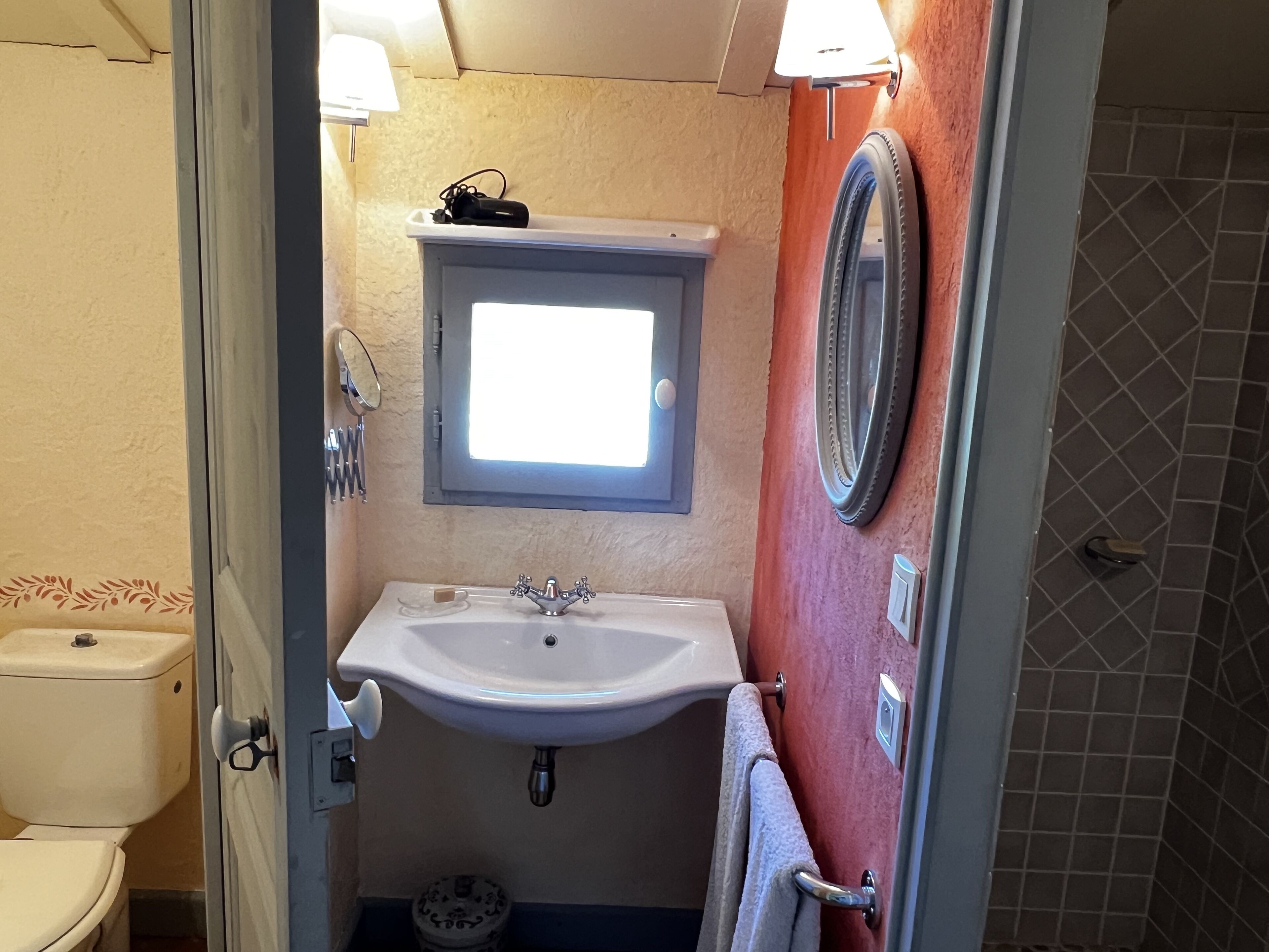 A bathroom with a white sink, a mirror, a toilet, and a window.