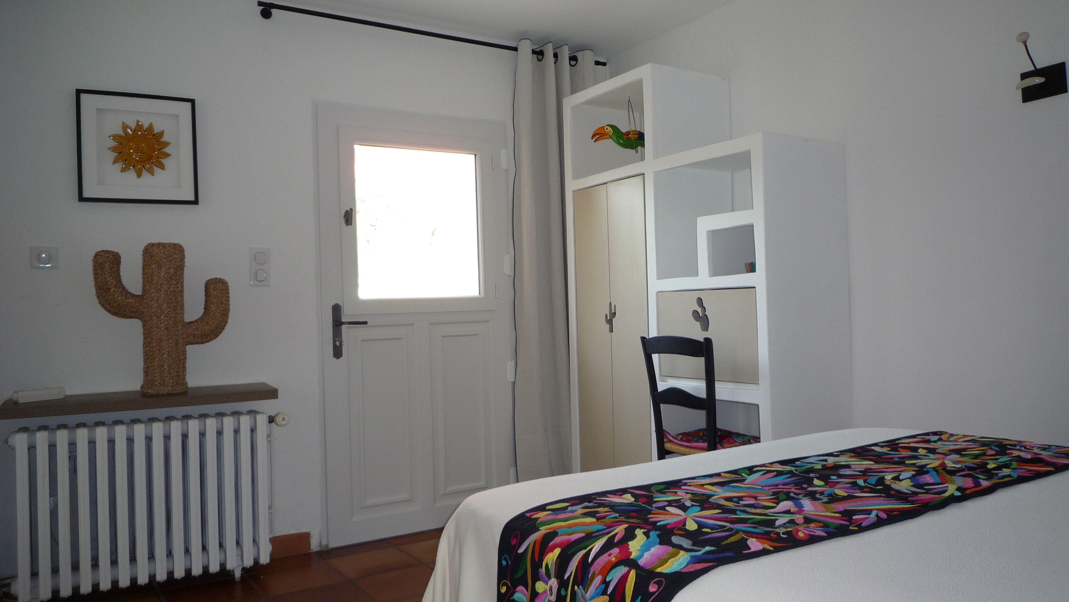 Ein Schlafzimmer mit Bett, Heizkörper, einer Kakteendekoration, einem Fenster und einem Kleiderschrank.