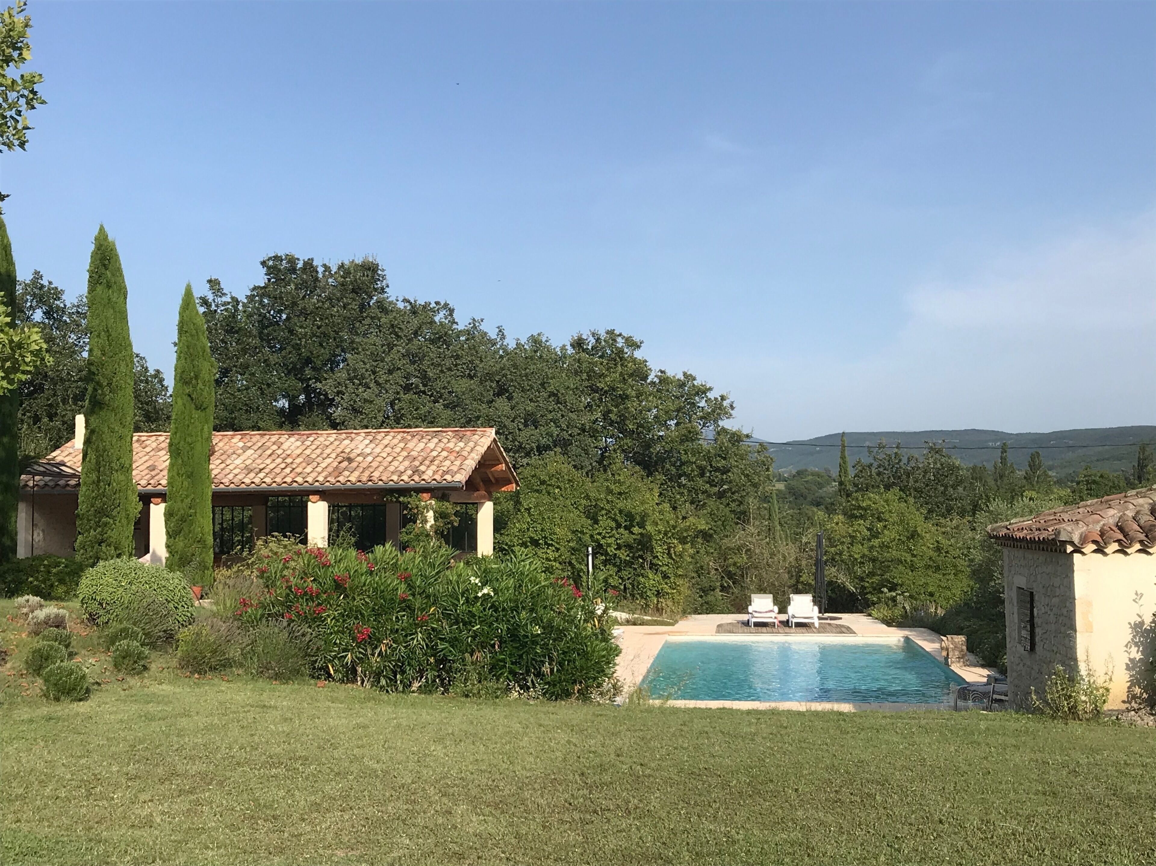 A villa with a swimming pool, surrounded by greenery and a clear view of the hills.