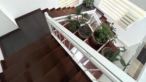 Una scala con ringhiera bianca, piante in vaso e un dipinto di un paesaggio urbano sulla parete.