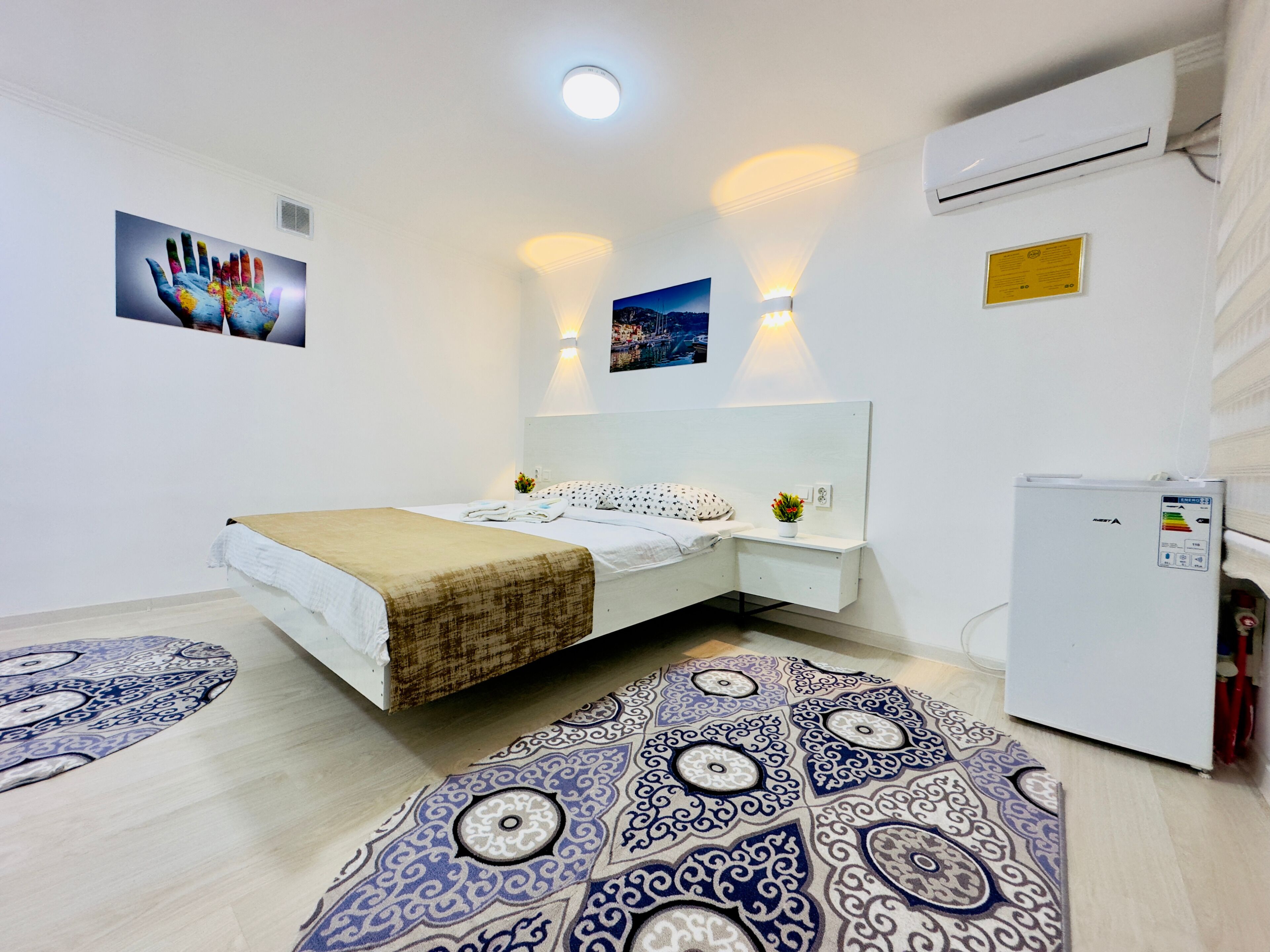 A modern bedroom with a bed, bedside tables, a wall-mounted air conditioner, and patterned rugs.