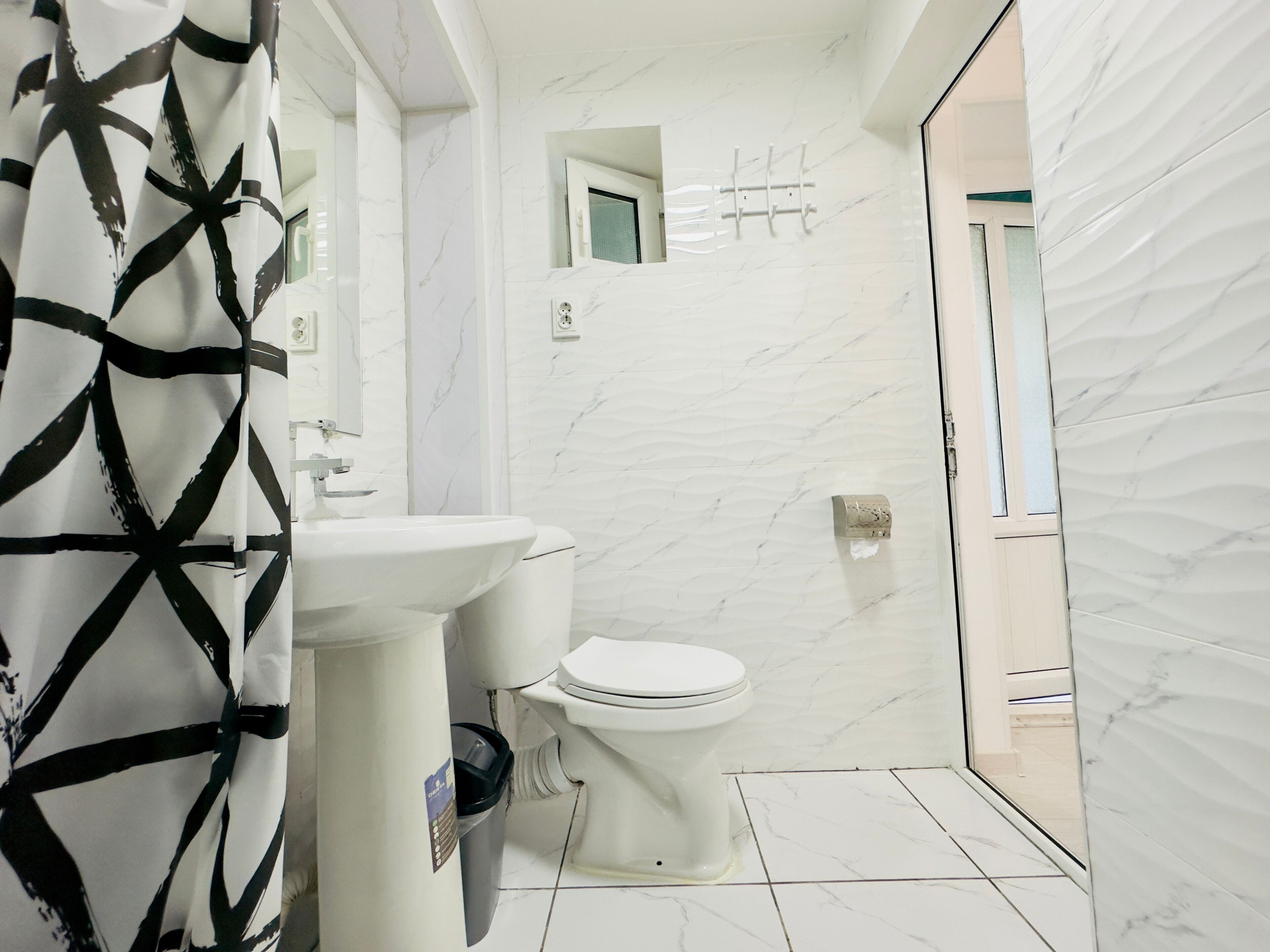 A bathroom with a white sink, toilet, and a mirror above the sink. There is a shower area visible through an open door.