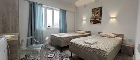 A hotel room with two beds, a desk, a chair, a patterned rug, and a world map poster.