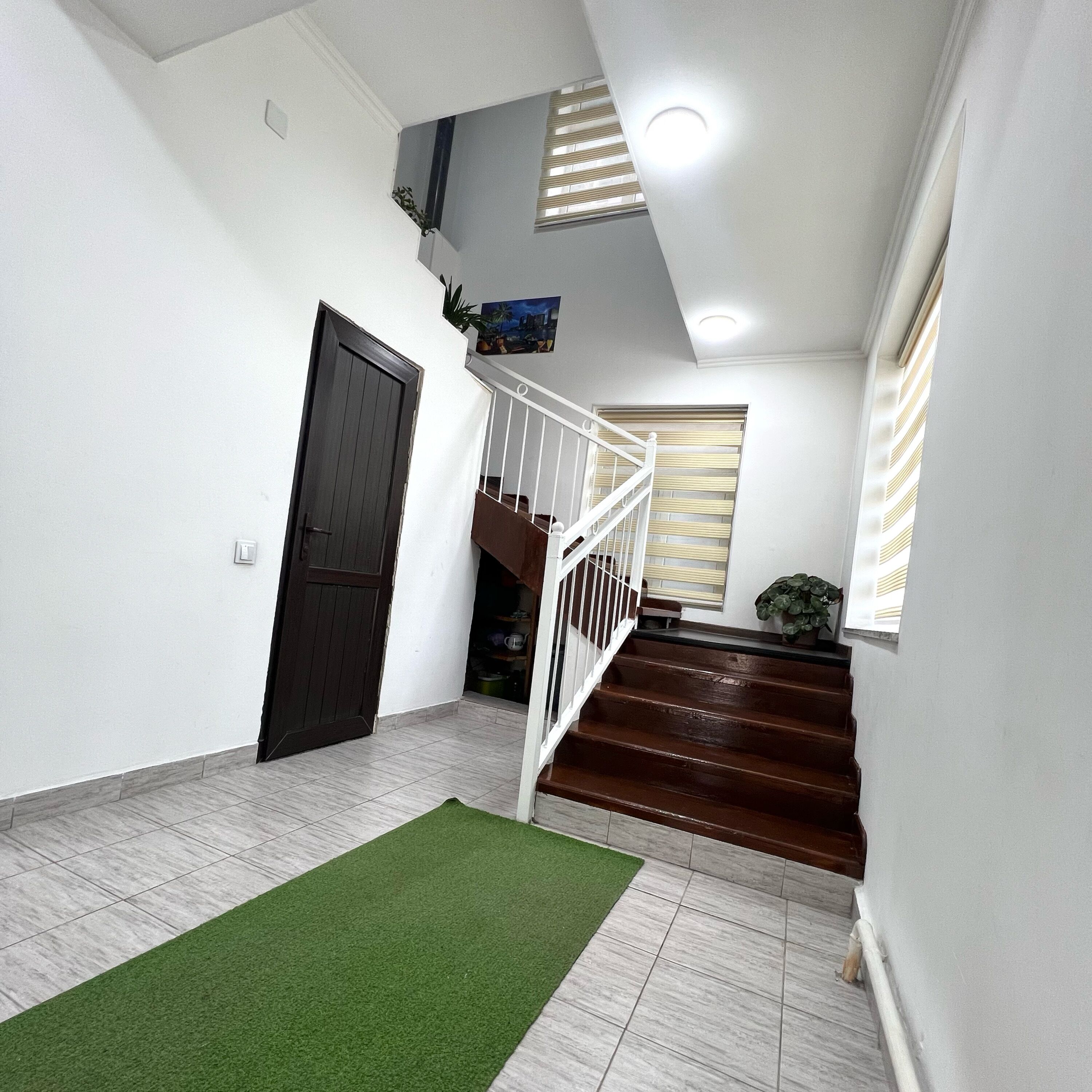 A staircase with a white railing, a dark wooden door, and a green rug on a tiled floor.