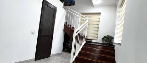 A staircase with a white railing, a dark wooden door, and a green rug on a tiled floor.
