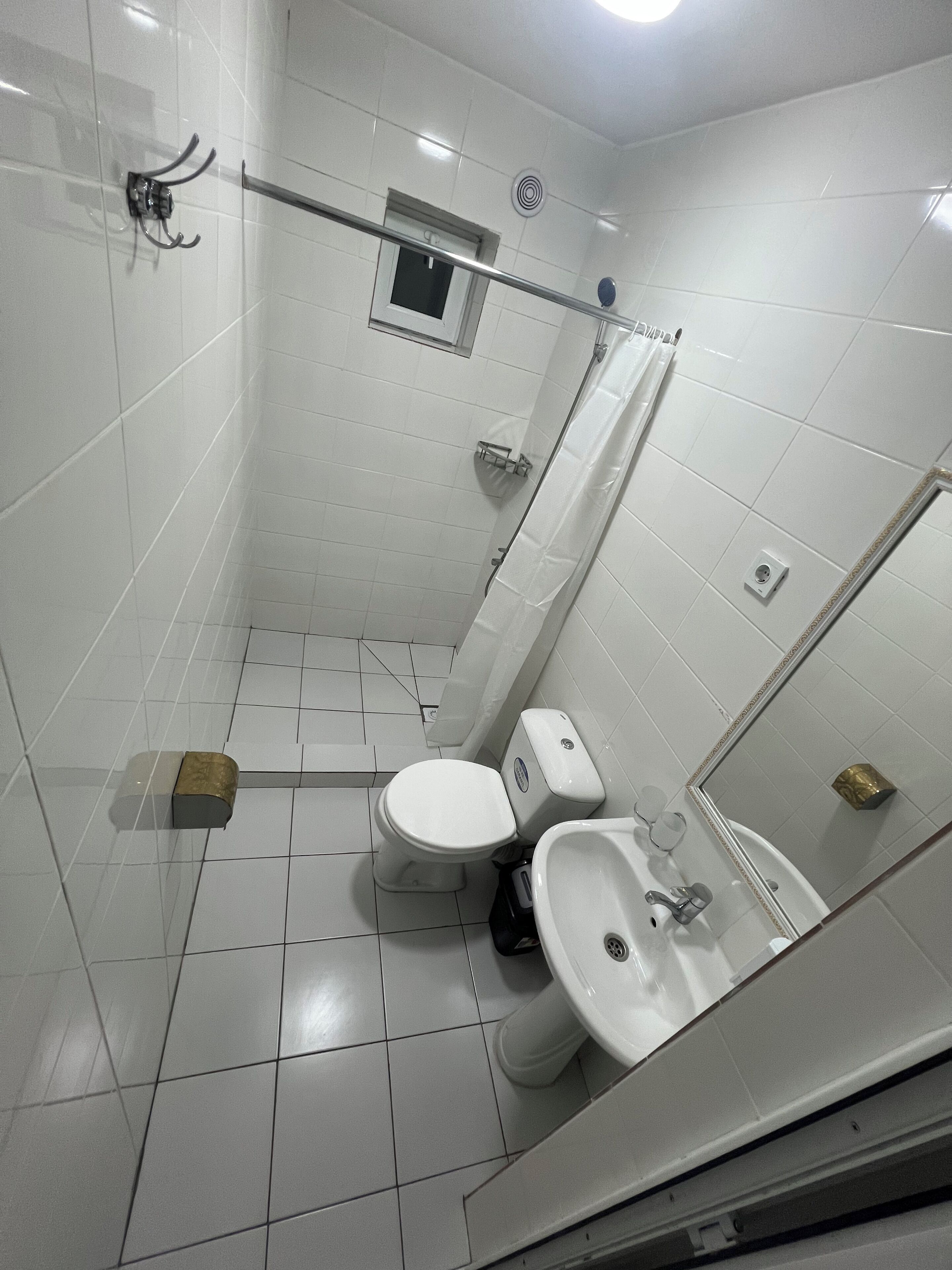 A bathroom with white tiled walls, a toilet, a sink, and a shower area.