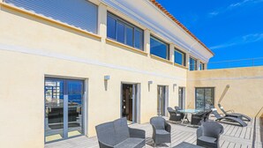 Ein modernes Gebäude mit flachem Dach, großen Fenstern und einer Terrasse mit Gartenmöbeln.