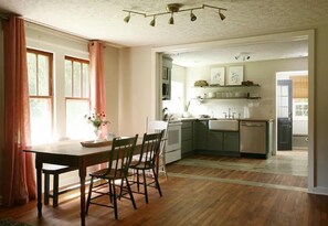 Une cuisine avec un plancher en bois, une table à manger avec des chaises, et une vue sur la salle à manger adjacente.