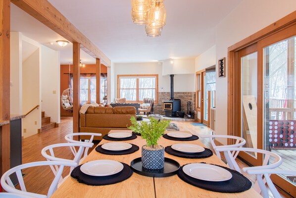 Comedor con una mesa de madera dispuesta para seis personas, rodeado de sillas blancas. Una planta en maceta está en el centro de la mesa.