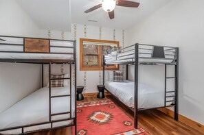 Een studentenkamer met stapelbedden, een plafondventilator, een raam met uitzicht en een kamerkleed met een patroon.